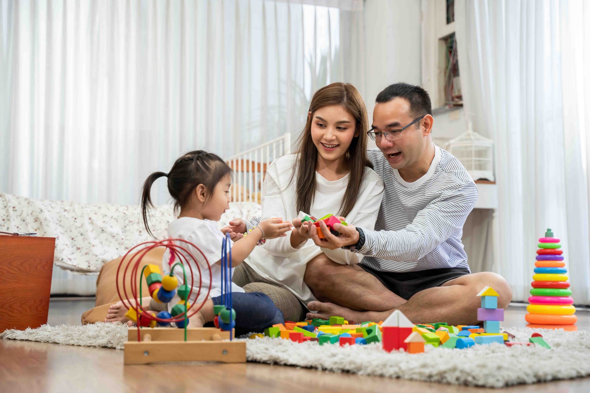 Happy young father and mother and a little daughter playing with Toy wooden blocks, sitting on the floor in living room, family, parenthood and people concept with Developmental toys